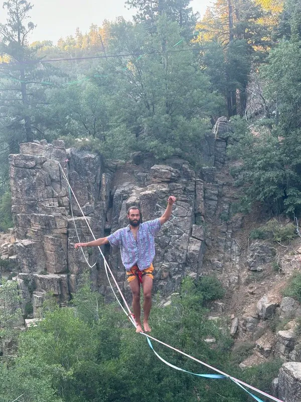 A photo of me working on a computer in a kitchen with a t-shirt covering my nose. My feet are holding up the laptop and Jordan is in the background looking at me. He's wearing a metal shirt.